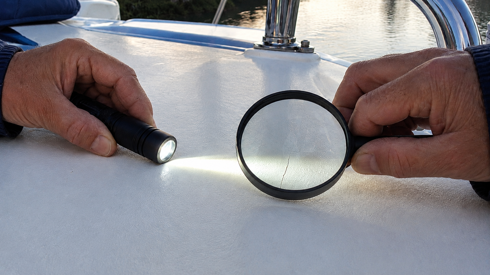 Hands using a flashlight and magnifying glass to inspect a crack in a fiberglass deck
