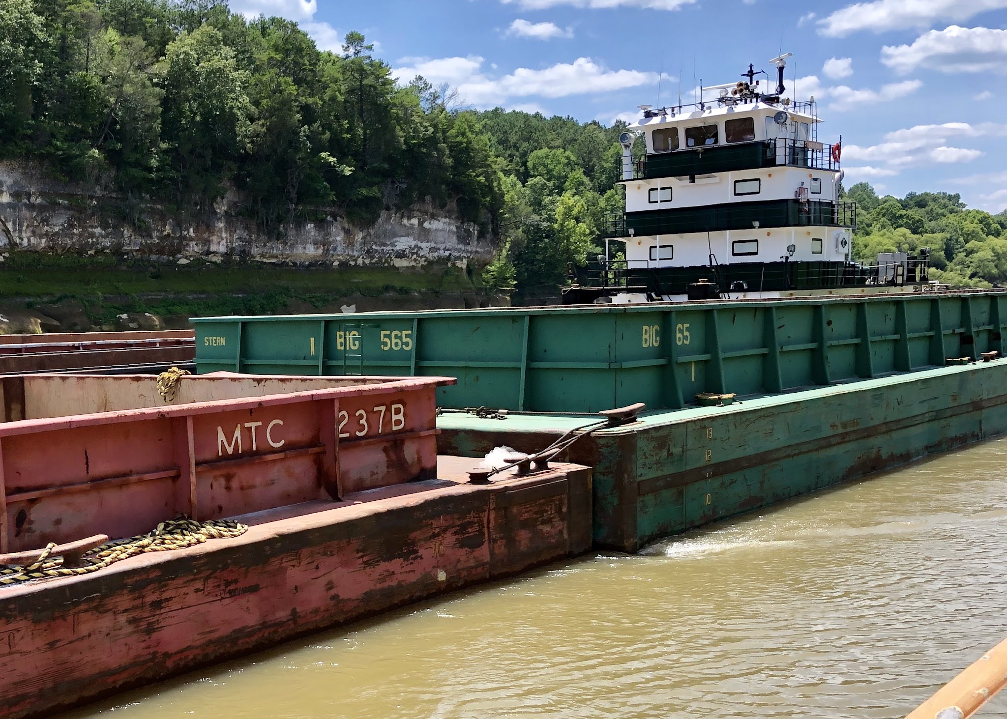 A towboat pushing loaded barges at close range on a narrow stretch of river